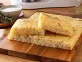 Focaccia senza glutine soffice e dorata, guarnita con rosmarino fresco, pronta per essere gustata.