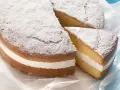 Torta paradiso sofficissima, con crema bianca e zucchero a velo. Una fetta è stata tagliata, invitando a gustarla.