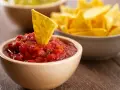 Una tortilla croccante affonda in una ciotola di fresca salsa messicana per tortillas, con altre tortillas sullo sfondo.