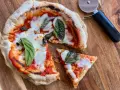 Pizza in padella appena sfornata, con pomodoro, mozzarella filante e basilico fresco, pronta per essere tagliata.