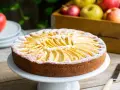 Torta di mele velocissima in 10 minuti, decorata con fettine di mela e zucchero a velo. Sullo sfondo, una cassetta di mele rosse e gialle.