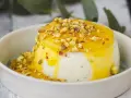 Budino fatto in casa cremoso, con salsa gialla e granella di pistacchi, servito in una ciotola bianca.