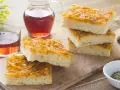 Focaccia con cipolle dorate e soffice, servita su un tagliere di legno con un bicchiere di vino rosato.