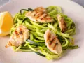 Spaghetti di zucchine con straccetti di pollo grigliato e una fetta di limone.