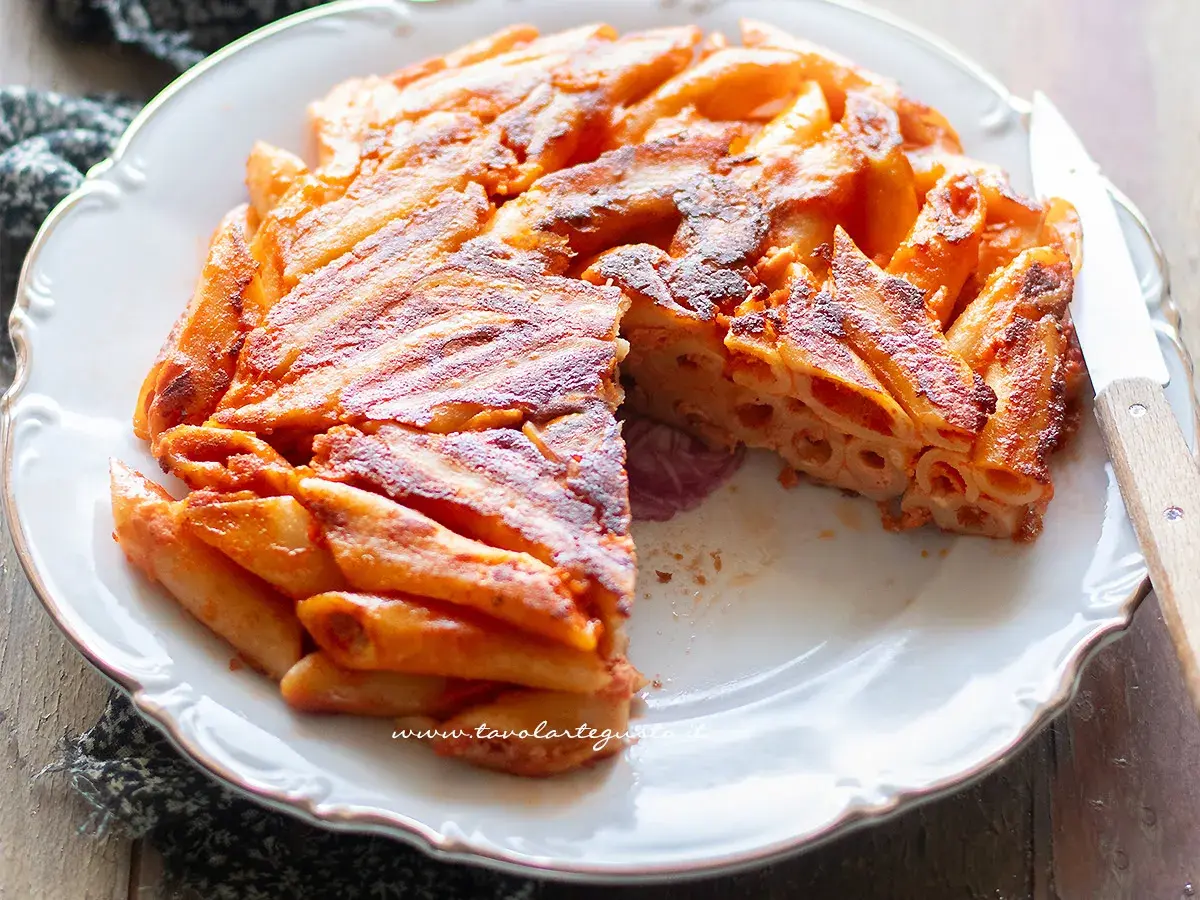 Una deliziosa frittata di maccheroni, dorata e croccante, servita su un piatto bianco con un coltello.