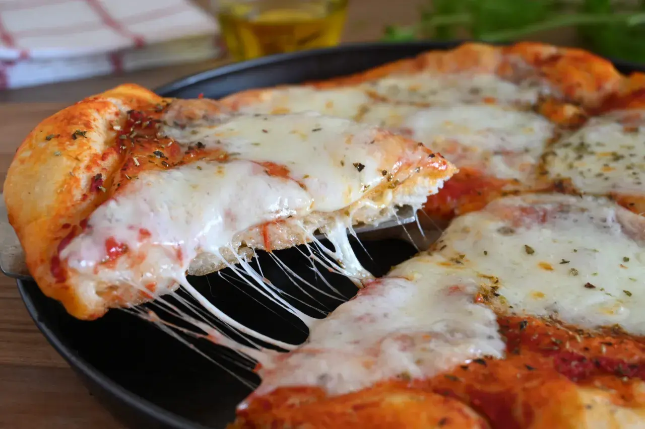 Una fetta di pizza fatta in casa con formaggio filante e crosta dorata, condita con erbe aromatiche.