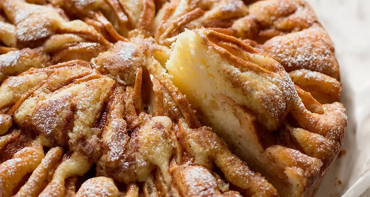 Una deliziosa torta di mele, cosparsa di zucchero a velo, con una fetta sollevata che mostra la morbida consistenza.
