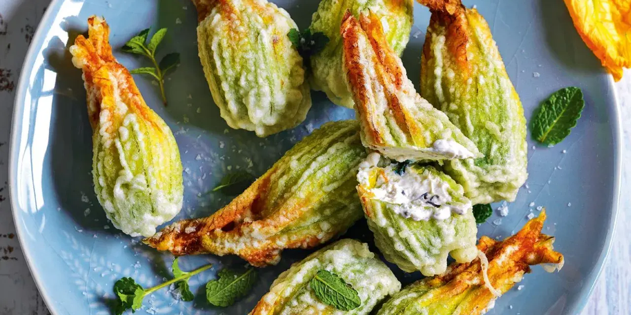 Fiori di zucca fritti, ripieni di formaggio cremoso e guarniti con foglie di menta fresca, su un piatto blu.