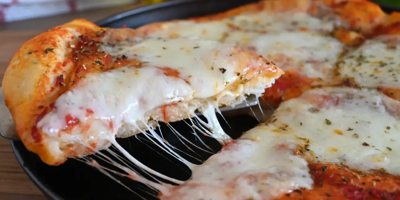 Una fetta di pizza fatta in casa con formaggio filante e crosta dorata, condita con erbe aromatiche.