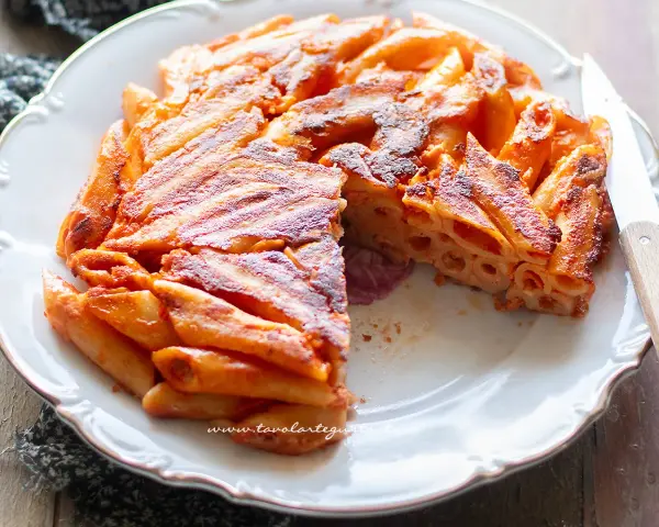 Una deliziosa frittata di maccheroni, dorata e croccante, servita su un piatto bianco con un coltello.