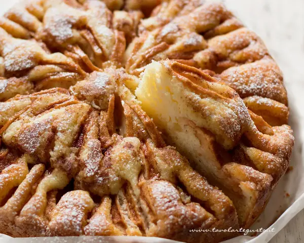 Una deliziosa torta di mele, cosparsa di zucchero a velo, con una fetta sollevata che mostra la morbida consistenza.
