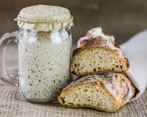 Un barattolo di rinfresco lievito madre accanto a fette di pane rustico.