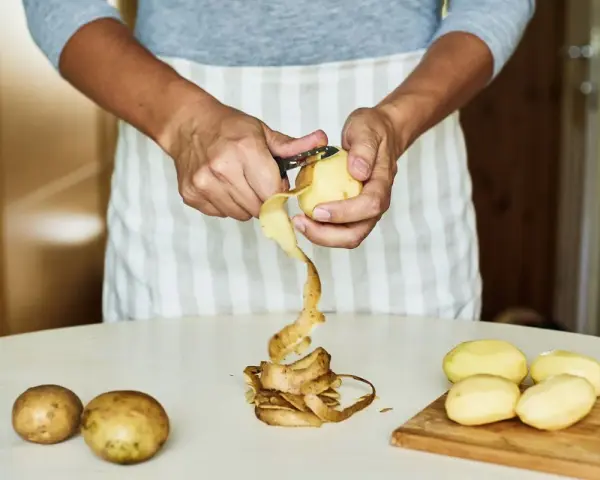 Mani che sbucciano patate per la cottura. Il tempo di cottura patate lesse senza buccia è breve.