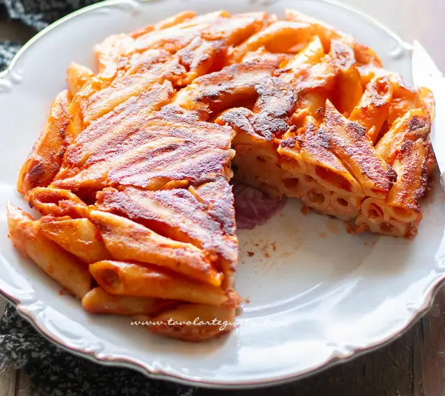 Una deliziosa frittata di maccheroni, dorata e croccante, servita su un piatto bianco con un coltello.