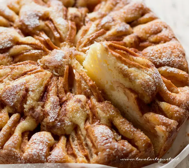 Una deliziosa torta di mele, cosparsa di zucchero a velo, con una fetta sollevata che mostra la morbida consistenza.