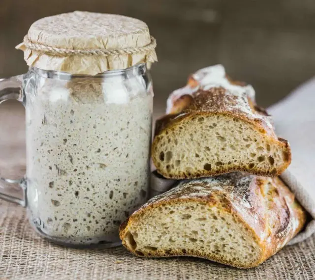 Un barattolo di rinfresco lievito madre accanto a fette di pane rustico.