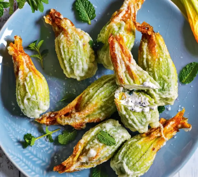 Fiori di zucca fritti, ripieni di formaggio cremoso e guarniti con foglie di menta fresca, su un piatto blu.