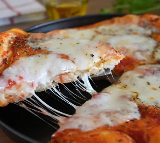 Una fetta di pizza fatta in casa con formaggio filante e crosta dorata, condita con erbe aromatiche.