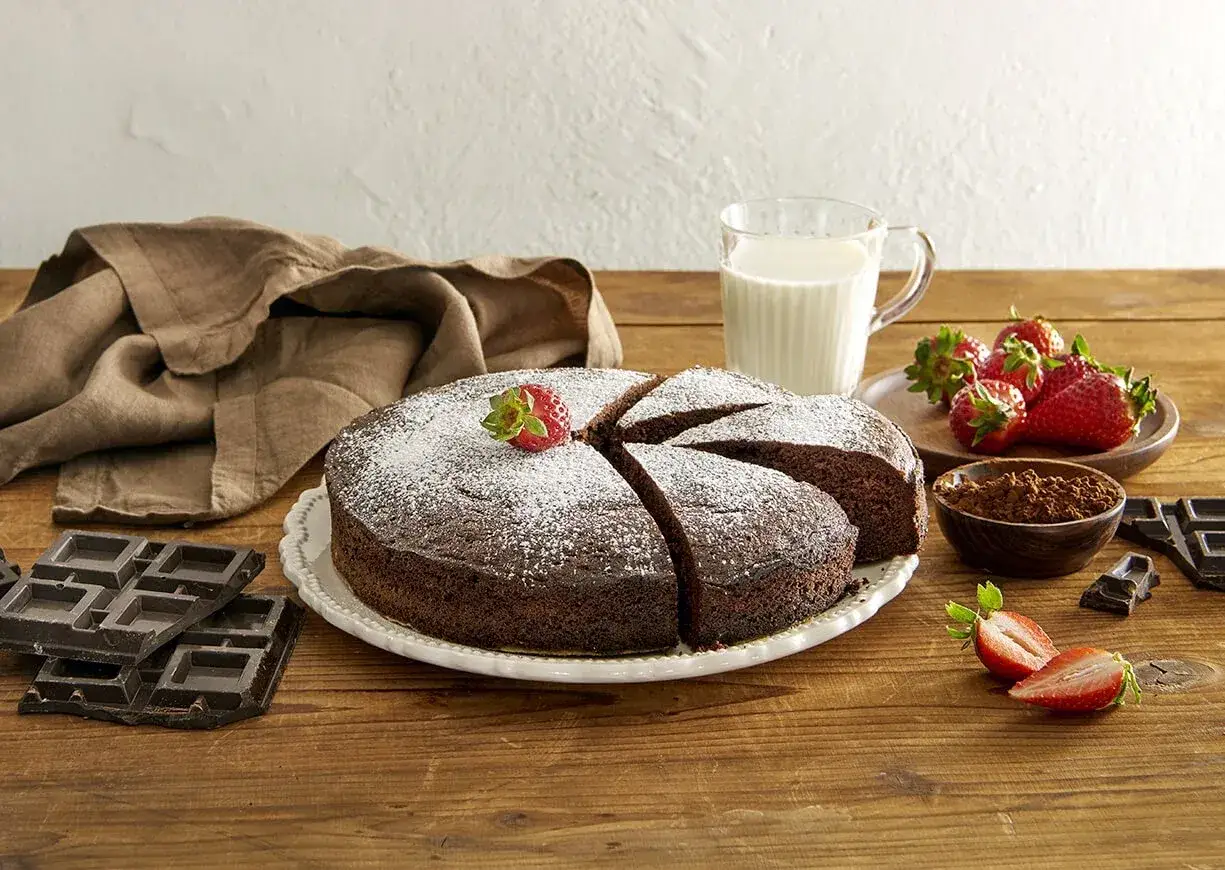 Una deliziosa torta al cioccolato, cosparsa di zucchero a velo e guarnita con una fragola, pronta per essere gustata con latte e fragole fresche.