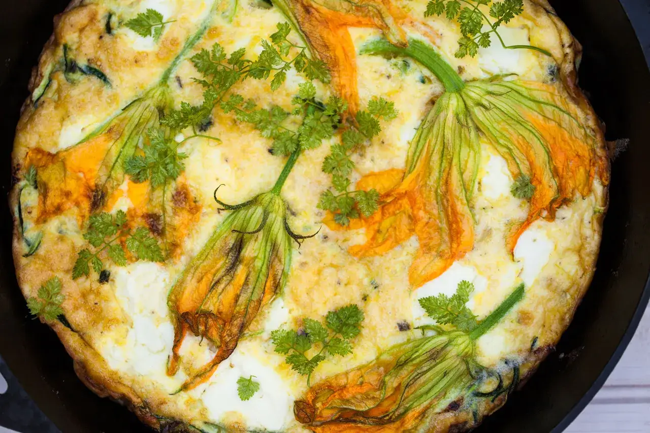 Frittata dorata con fiori di zucca freschi e prezzemolo, un piatto primaverile invitante.
