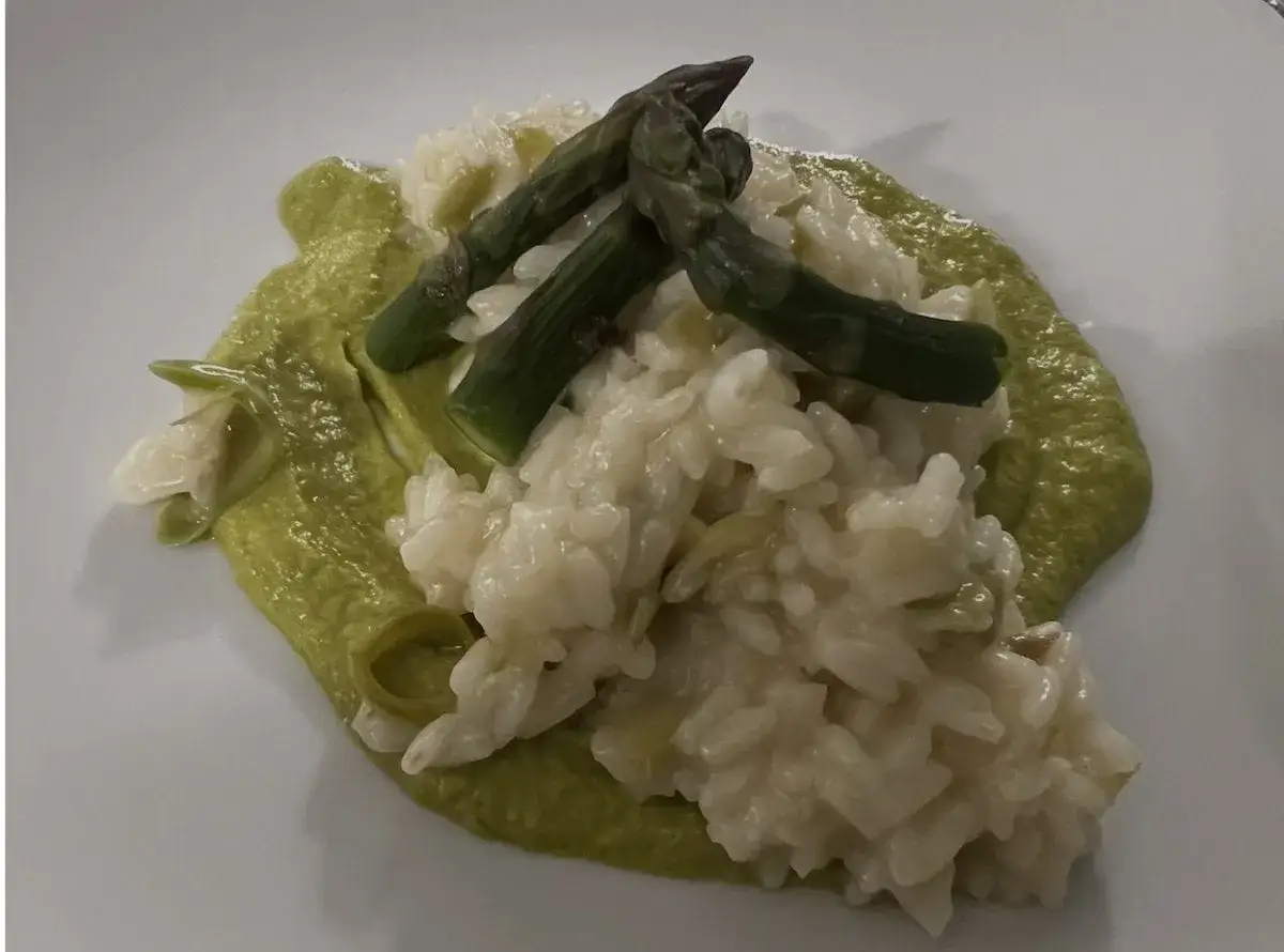 Un cremoso risotto con asparagi, guarnito con punte di asparagi freschi e una vellutata verde brillante.