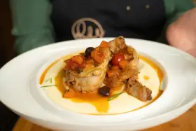 Pollo alla cacciatora succulento su un letto di polenta cremosa, guarnito con pomodorini, olive e carote.