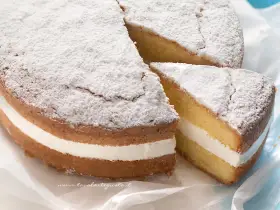Torta paradiso sofficissima, con crema bianca e zucchero a velo. Una fetta è stata tagliata, invitando a gustarla.