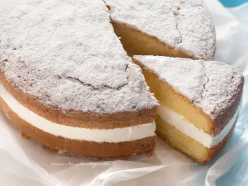 Torta paradiso sofficissima, con crema bianca e zucchero a velo. Una fetta è stata tagliata, invitando a gustarla.