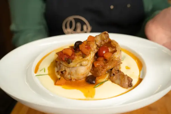 Pollo alla cacciatora succulento su un letto di polenta cremosa, guarnito con pomodorini, olive e carote.