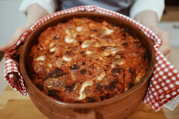Un invitante pasta al forno ricetta della nonna, appena sfornata in una terracotta, con crosticina dorata e ripieno filante.