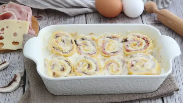 Nidi di rondine in una teglia bianca, con prosciutto, formaggio e funghi. Ingredienti per un piatto delizioso.