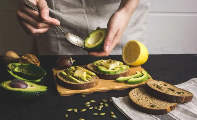 Preparazione di gustose ricette con avocado: toast con avocado, formaggio e semi.