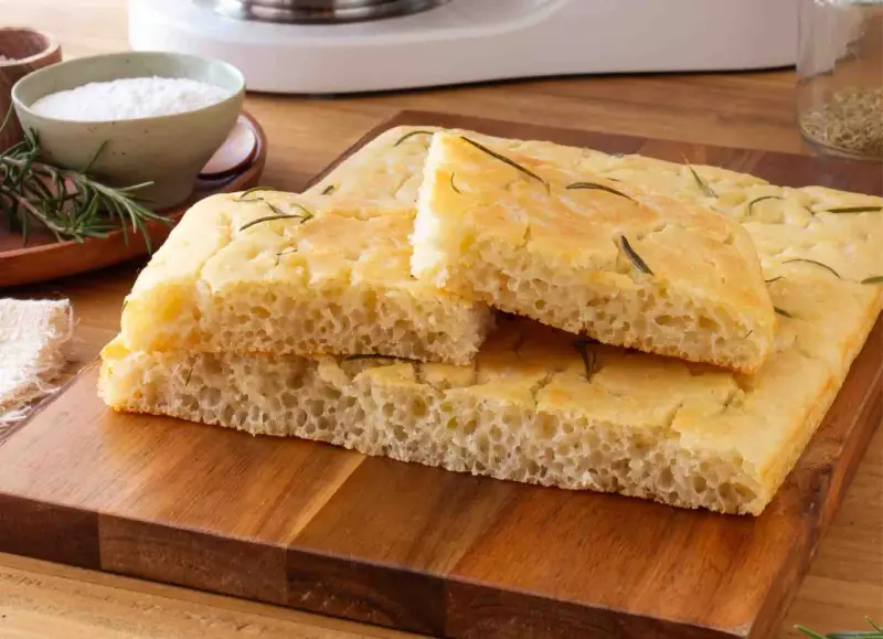 Focaccia senza glutine soffice e dorata, guarnita con rosmarino fresco, pronta per essere gustata.