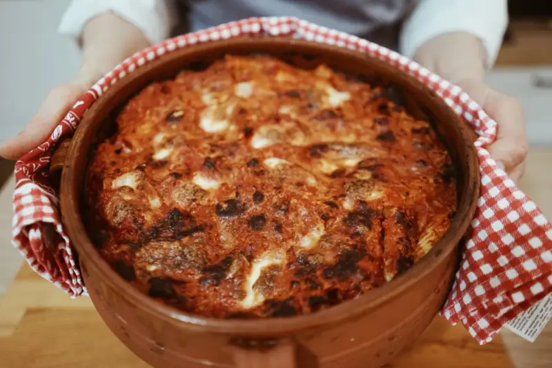 Un invitante pasta al forno ricetta della nonna, appena sfornata in una terracotta, con crosticina dorata e ripieno filante.
