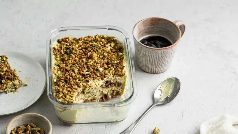 Un delizioso tiramisù al pistacchio, cosparso di granella verde, pronto per essere gustato con un caffè.