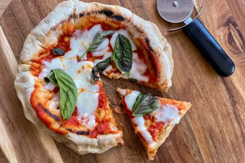 Pizza in padella appena sfornata, con pomodoro, mozzarella filante e basilico fresco, pronta per essere tagliata.
