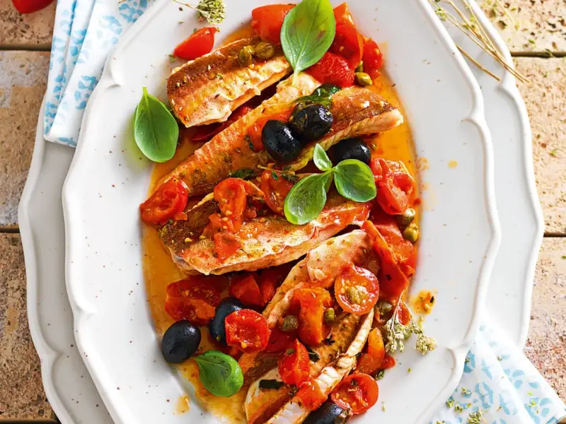 Deliziosa gallinella di mare in umido con pomodorini, olive nere e capperi, guarnita con basilico fresco.
