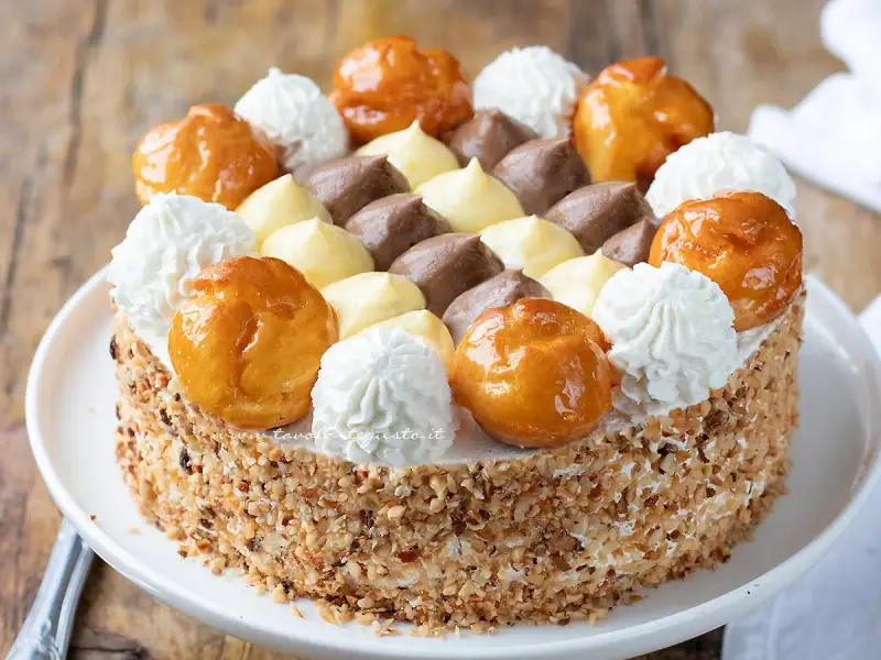 Una deliziosa torta Saint Honoré, con bignè caramellati, panna montata e crema al cioccolato e vaniglia, il tutto ricoperto di granella di nocciole.