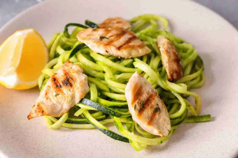 Spaghetti di zucchine con straccetti di pollo grigliato e una fetta di limone.
